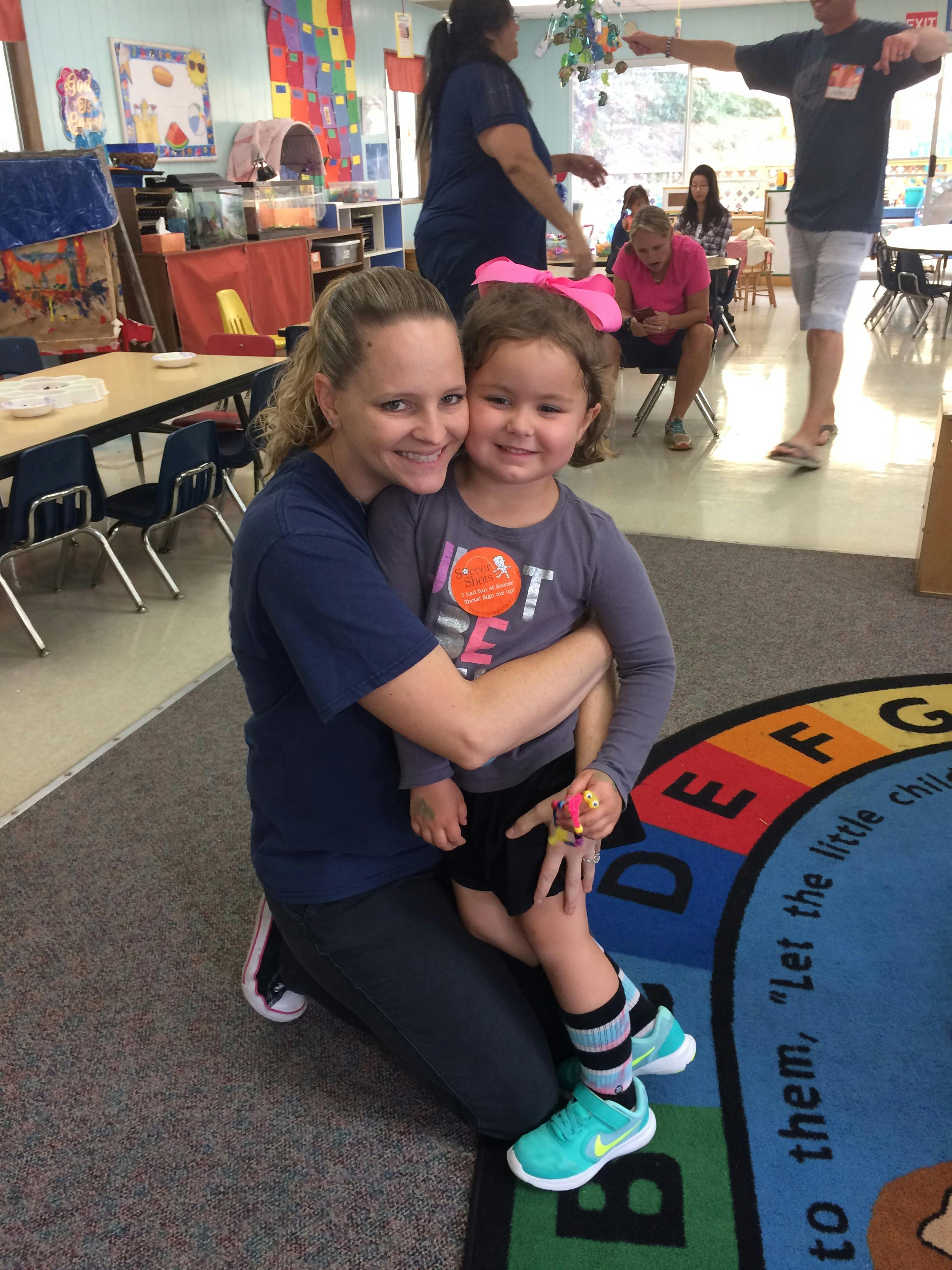 Person kneeling and hugging a child in a classroom