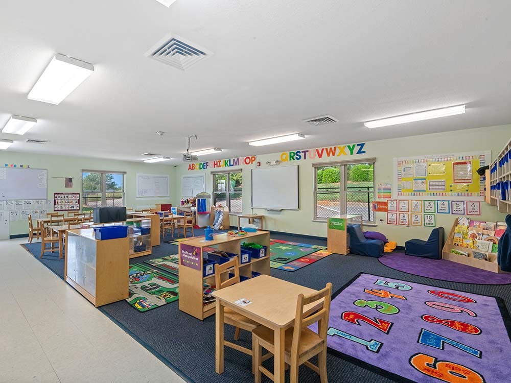 Empty classroom with small tables and chairs, and alphabet and number rugs