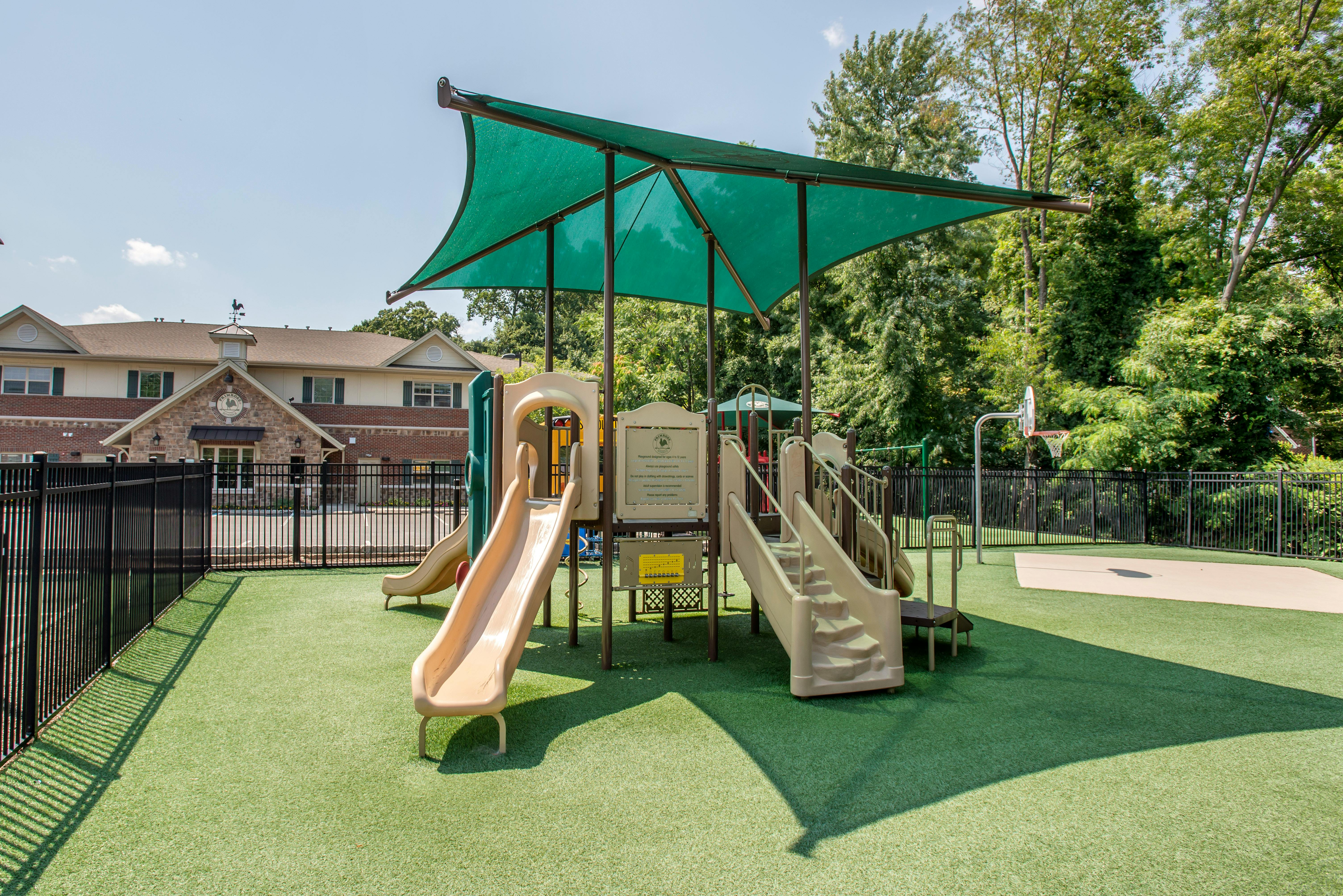 Playground with slides, stairs, and a green shade canopy over artificial grass