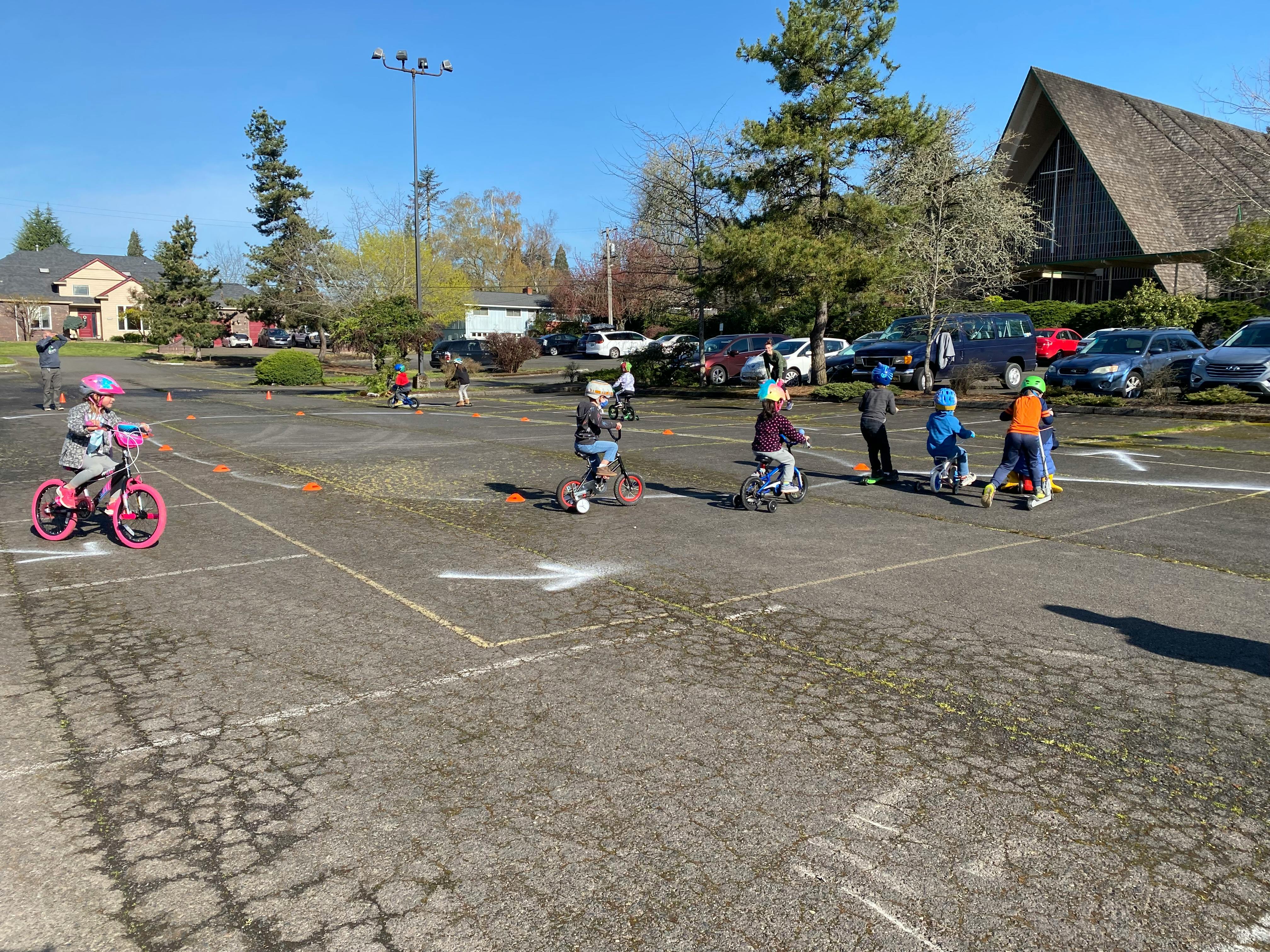 Children on bikes and scooters in a parking lot