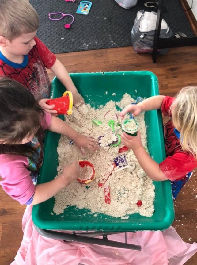 Three children playing with sand in a green bin