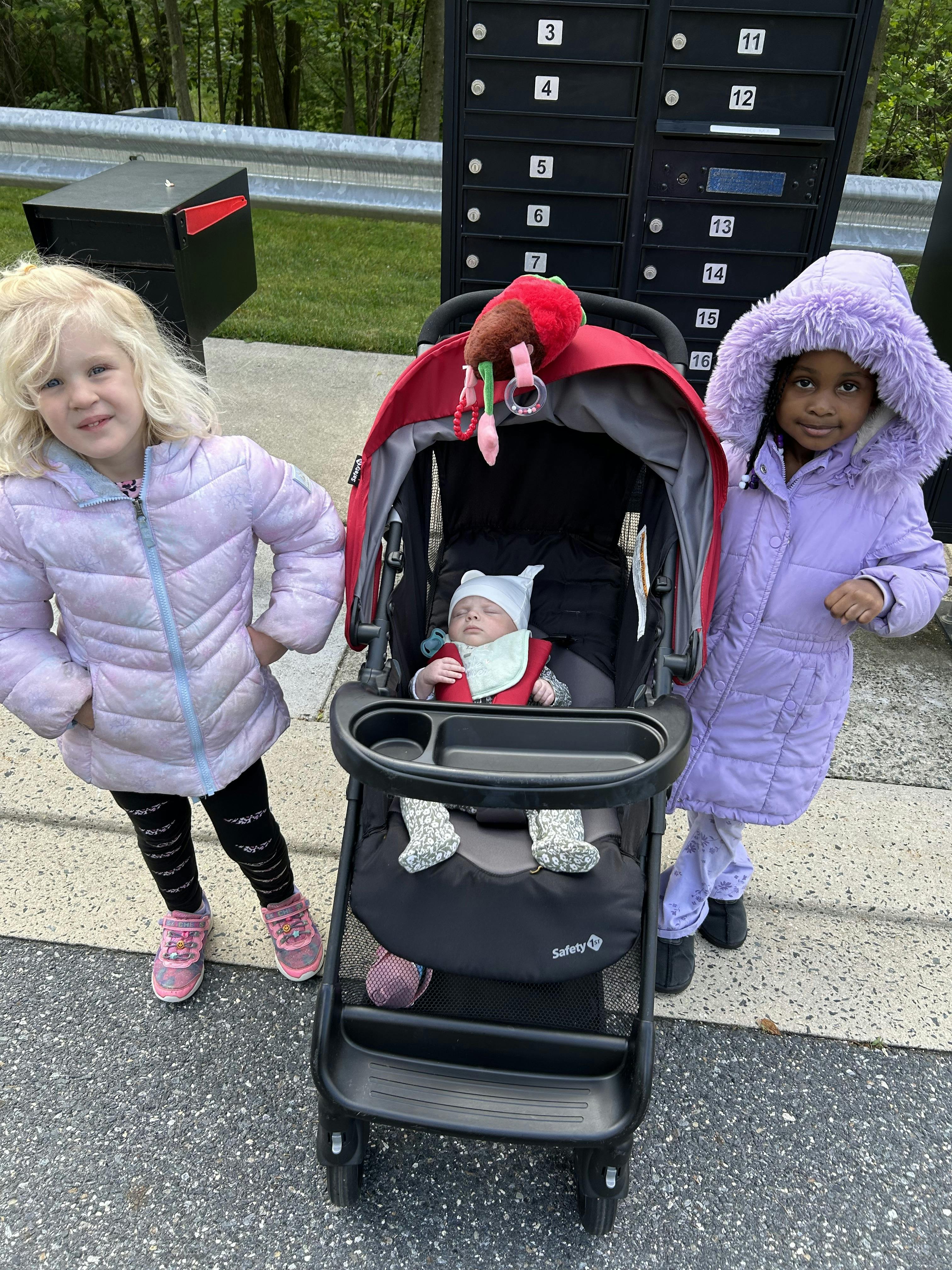 Two children standing next to a baby in a stroller outdoors