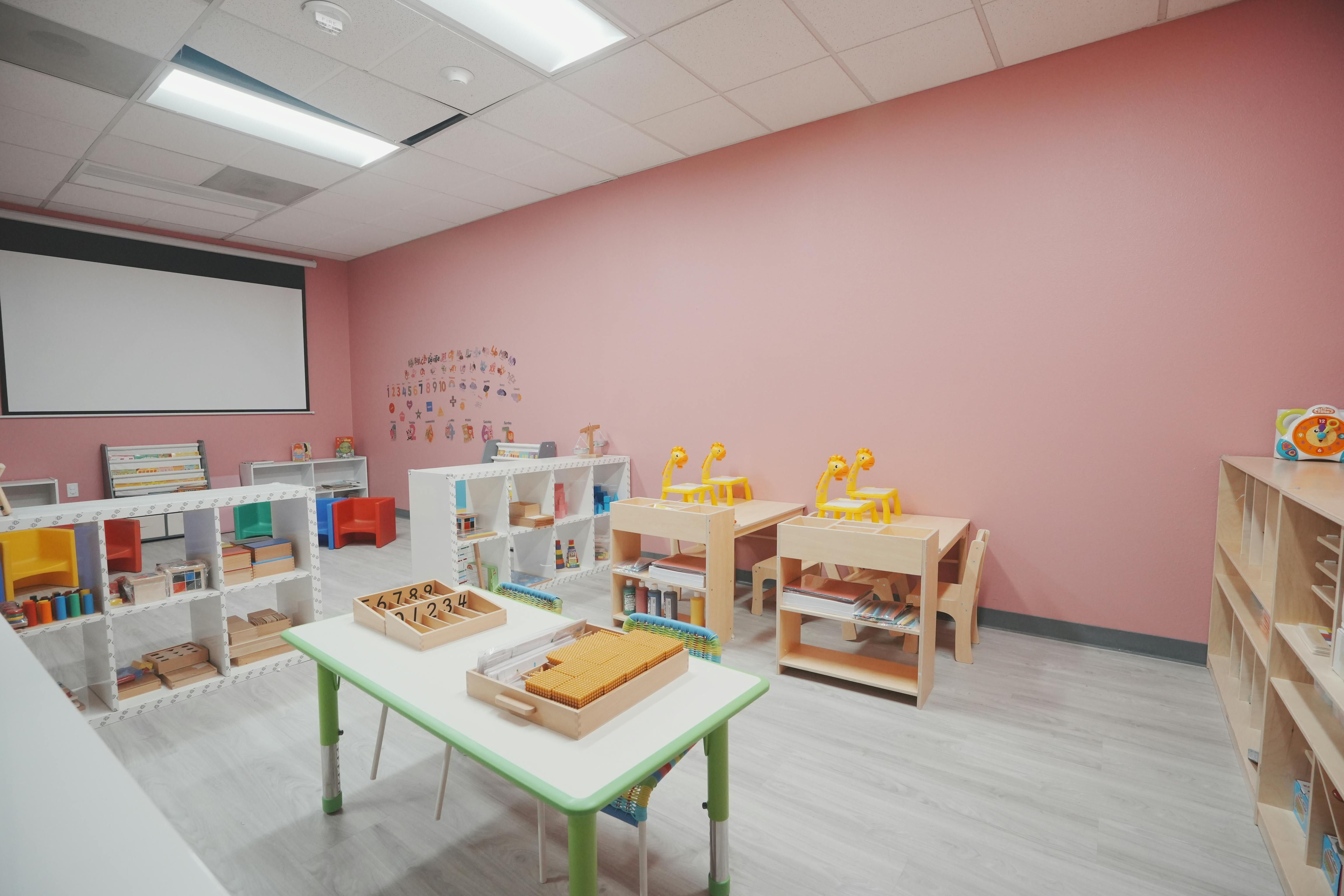 Classroom with pink walls, small tables, shelves with learning materials