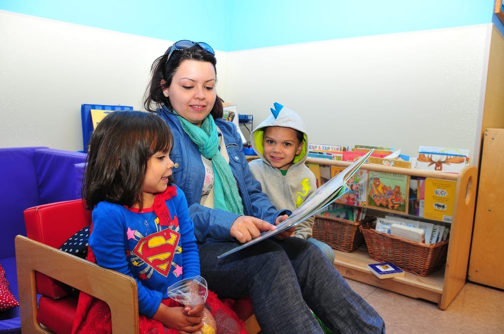 Person reading a book to two children in a classroom