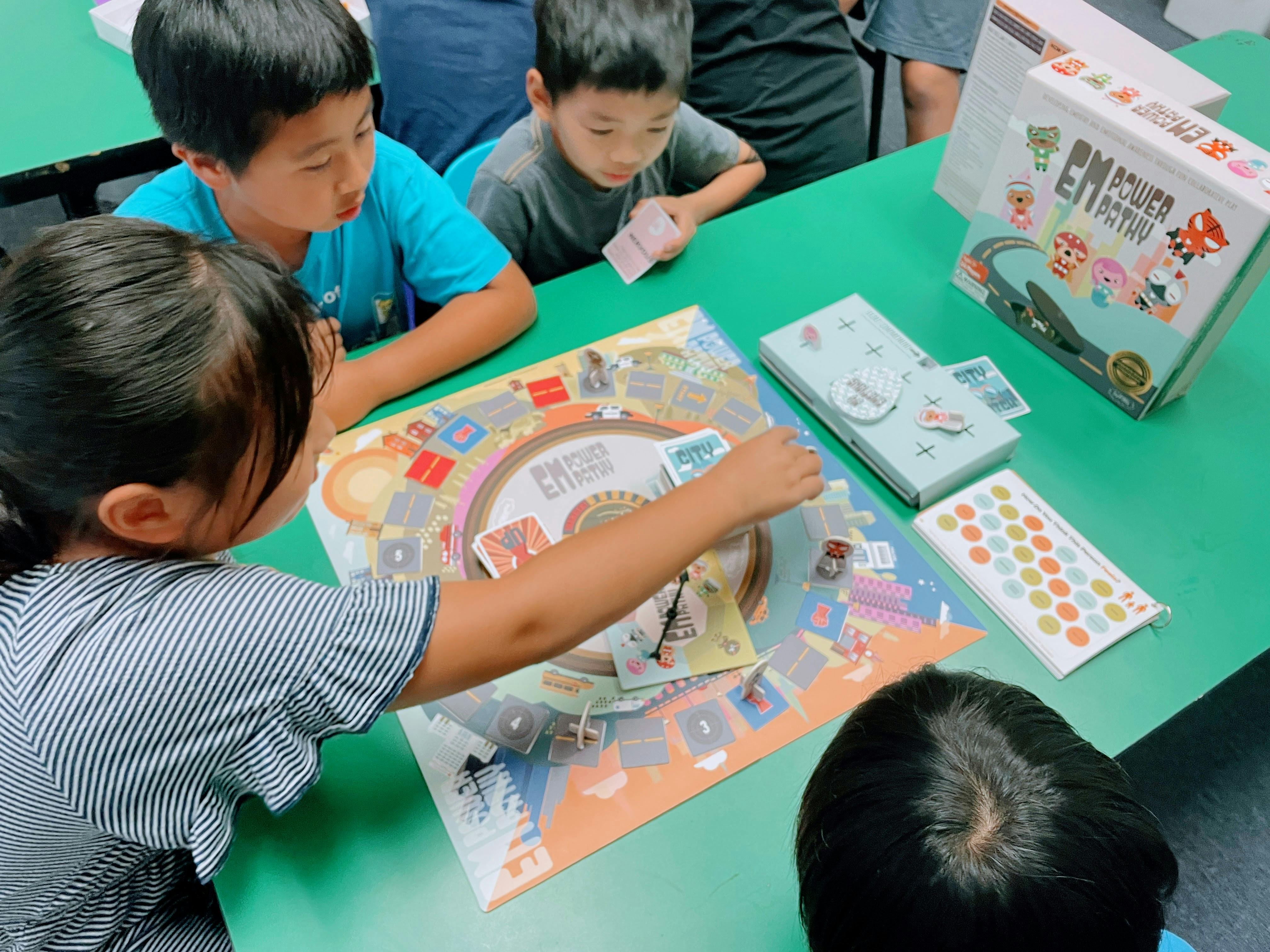 Children gathered around a table playing a board game called EMPOWER PATHY