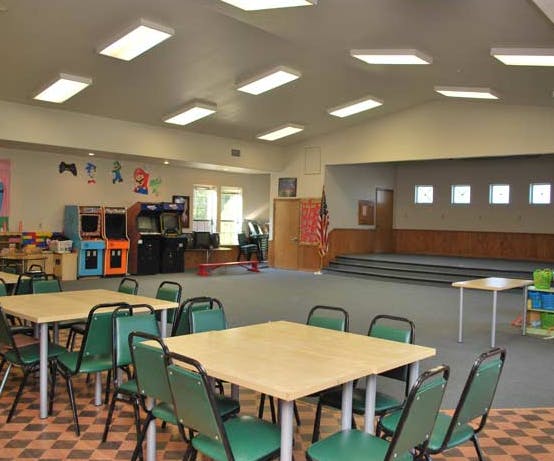 Room with tables and chairs in foreground, stage and arcade games in background