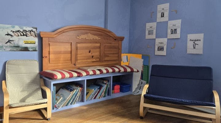 Room with blue walls, a wooden bench with cushions, bookshelves, and chairs