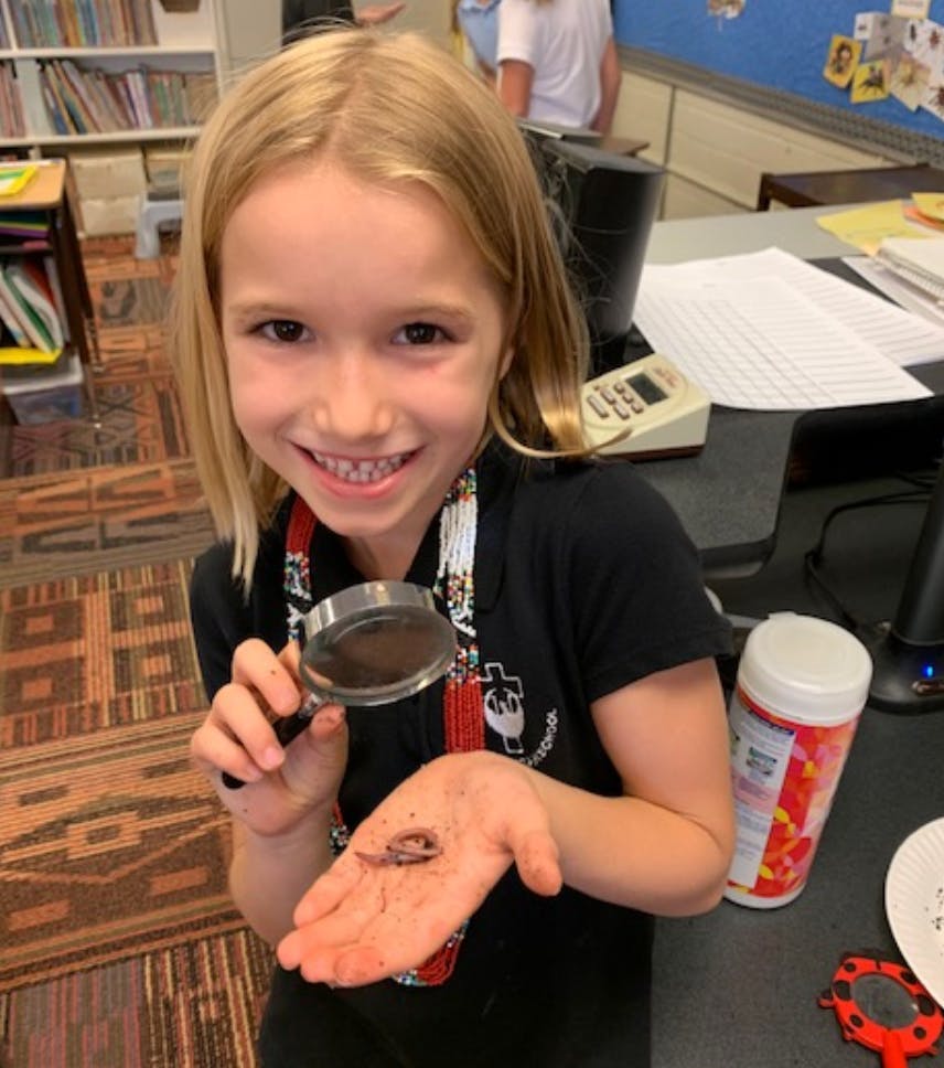 Child holding a magnifying glass over a worm in their hand