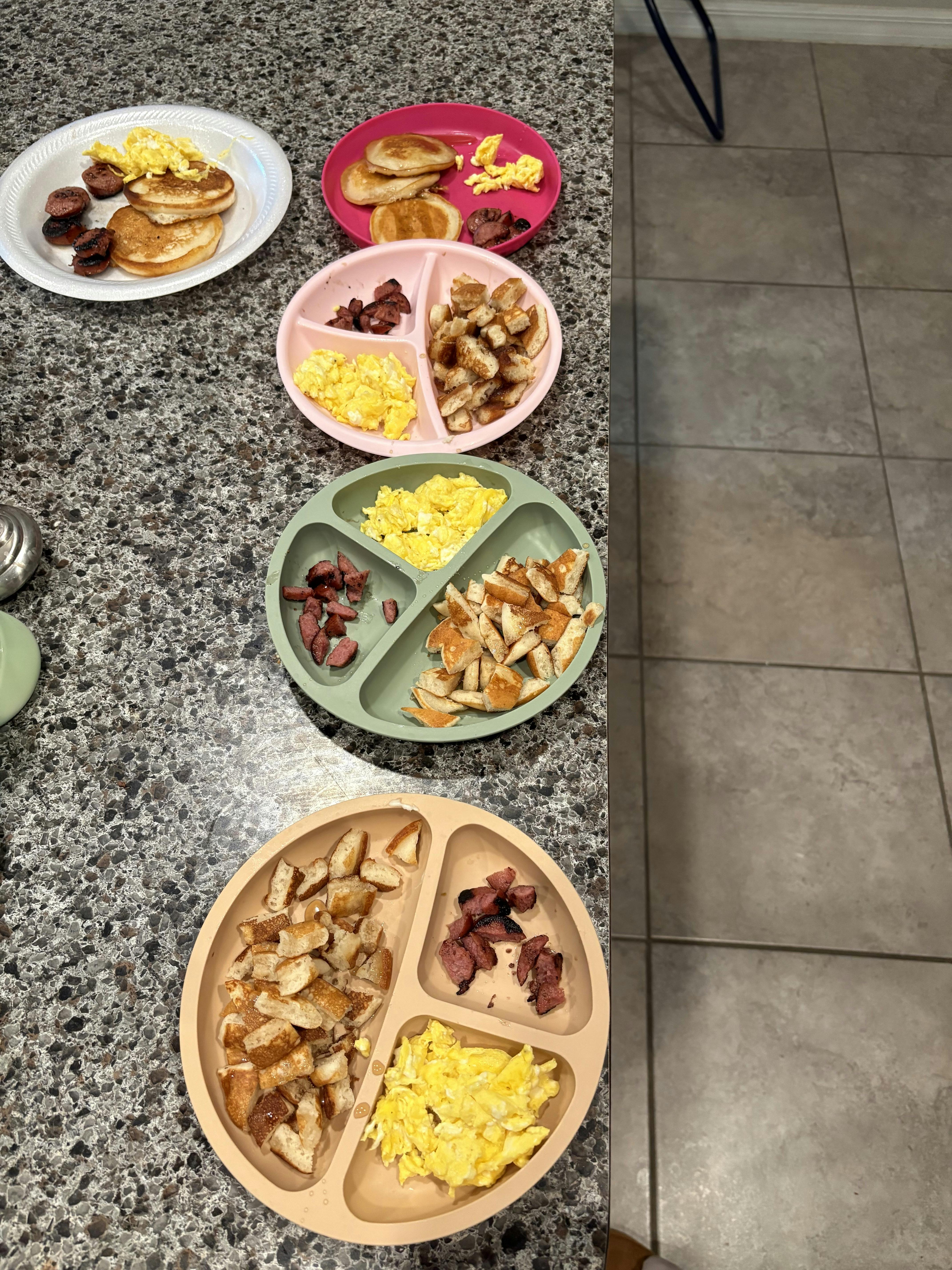 Multiple plates of breakfast food on a counter, including pancakes, scrambled eggs, and sausage