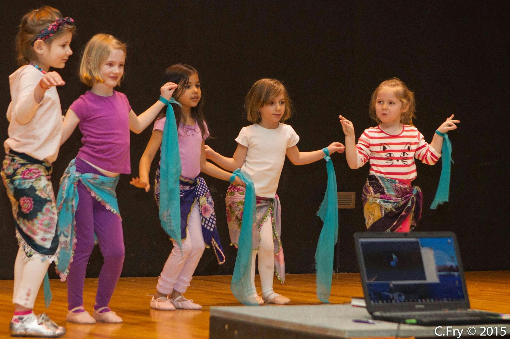 Five children dancing with blue scarves on a stage