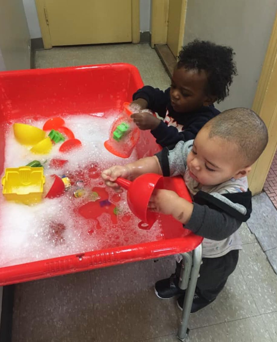 Two children playing with toys in a red bin filled with soapy water