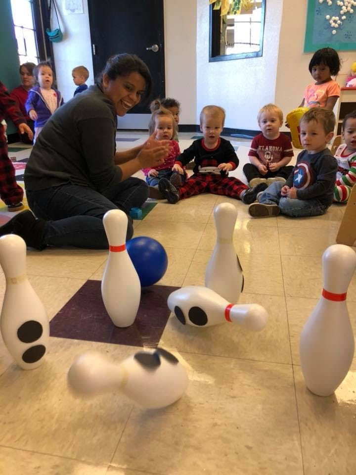 Adult and children sitting on floor with bowling pins and ball