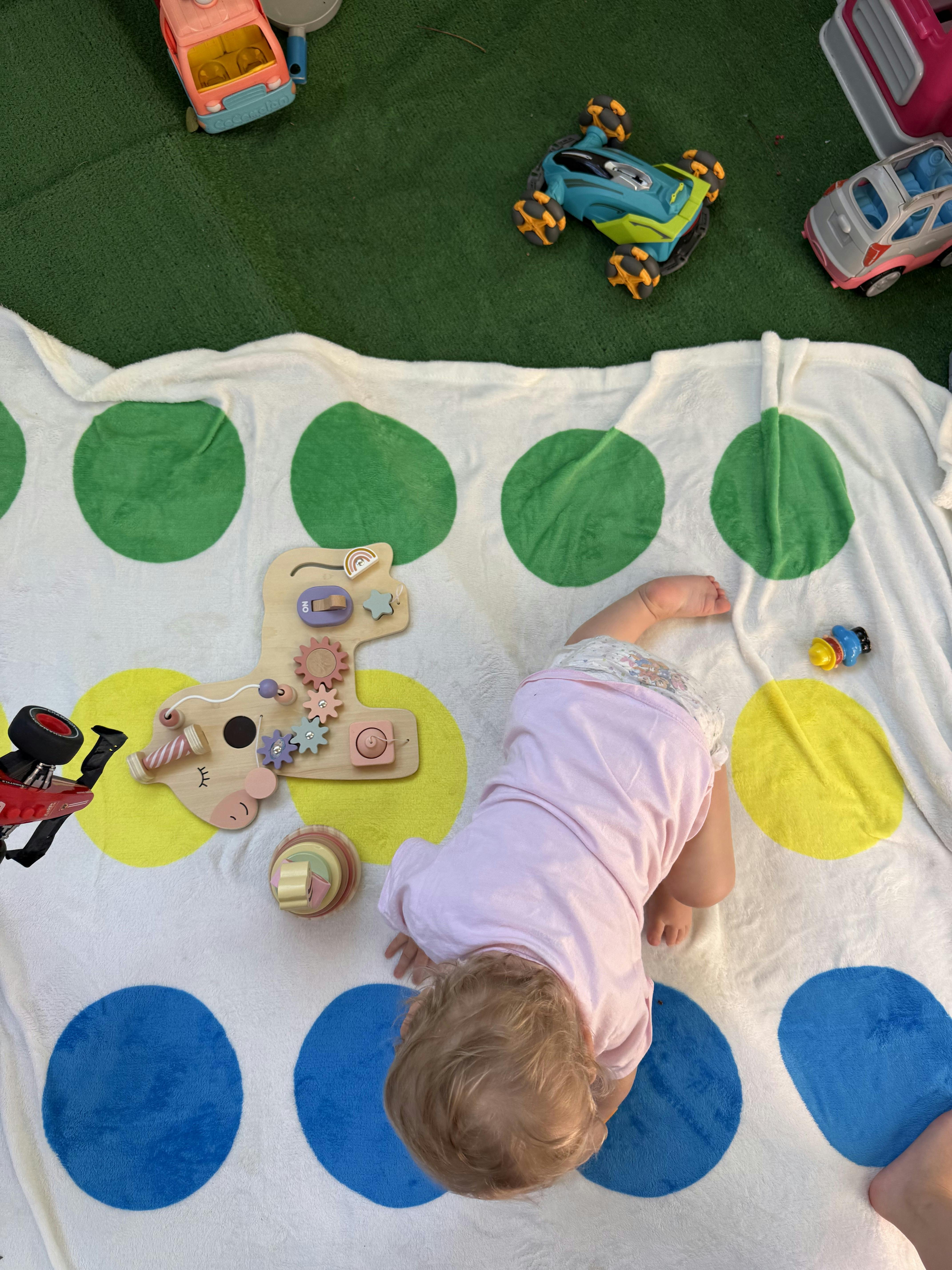 Child crawling on a dotted play mat with various toys