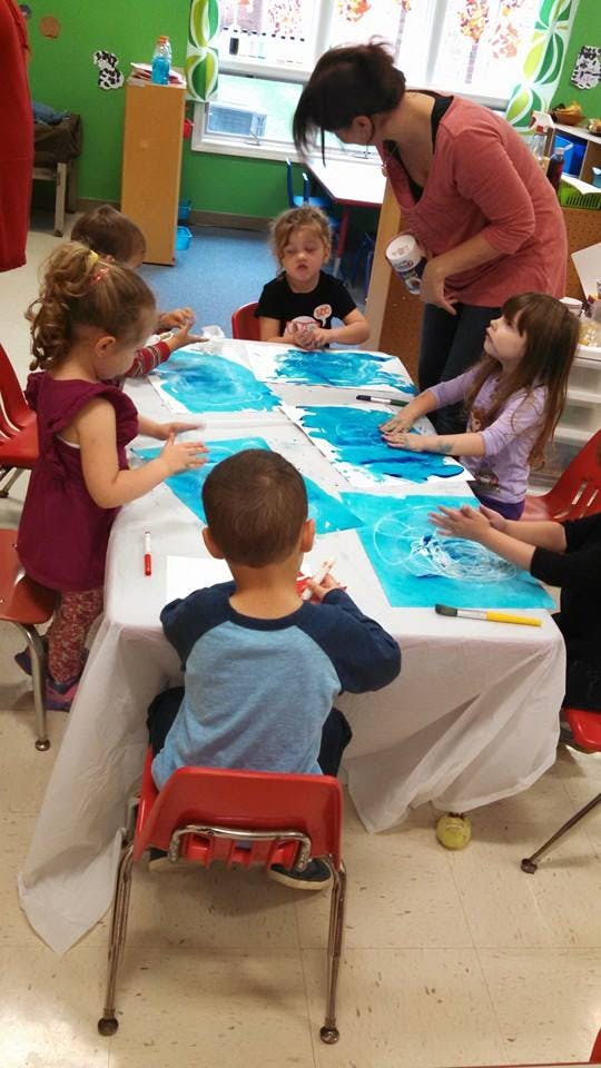 Adult and children painting at a table in a classroom