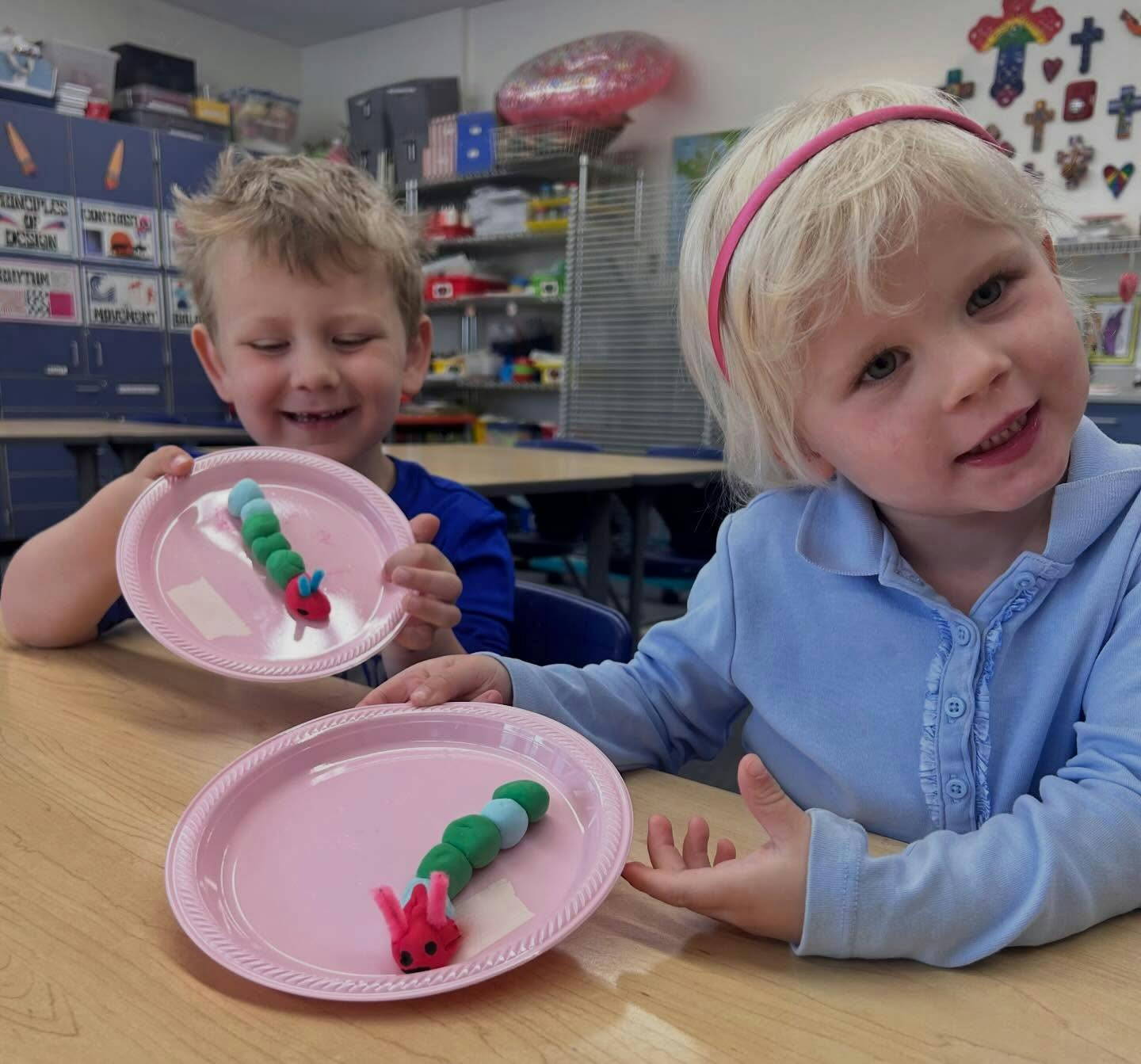 Two children with playdough caterpillars on pink plates in a classroom