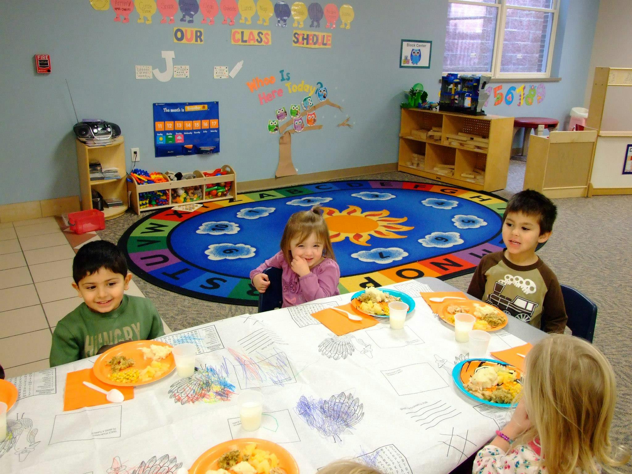 Children sitting at a table with plates of food in a classroom