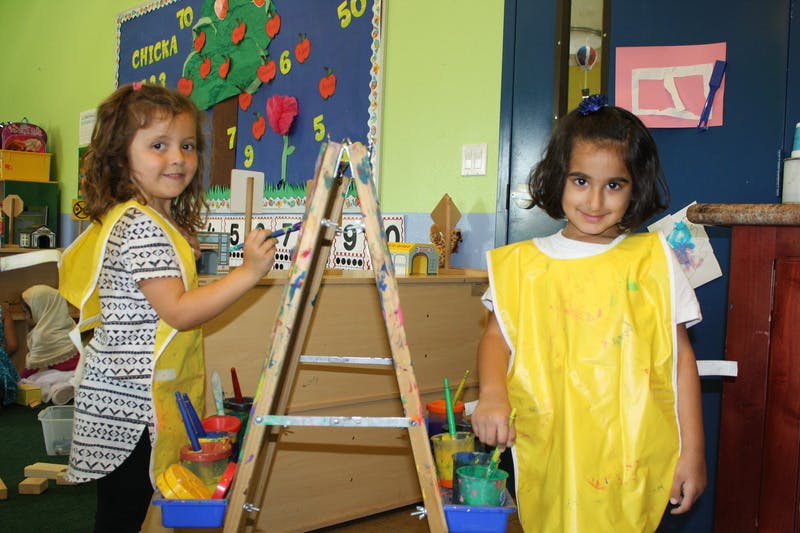Two children in yellow smocks painting on an easel in a classroom