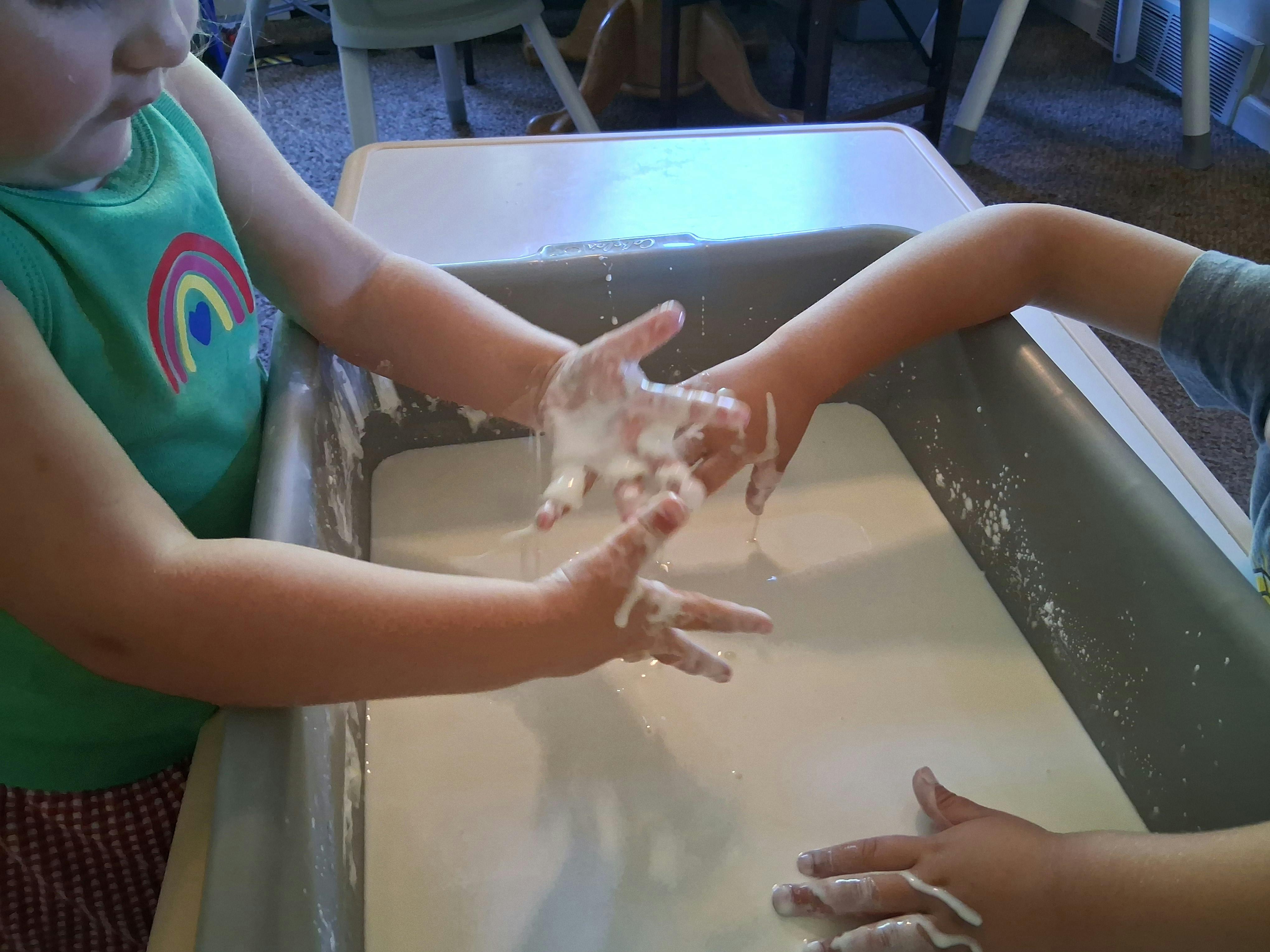 Children playing with white sensory liquid in a plastic bin