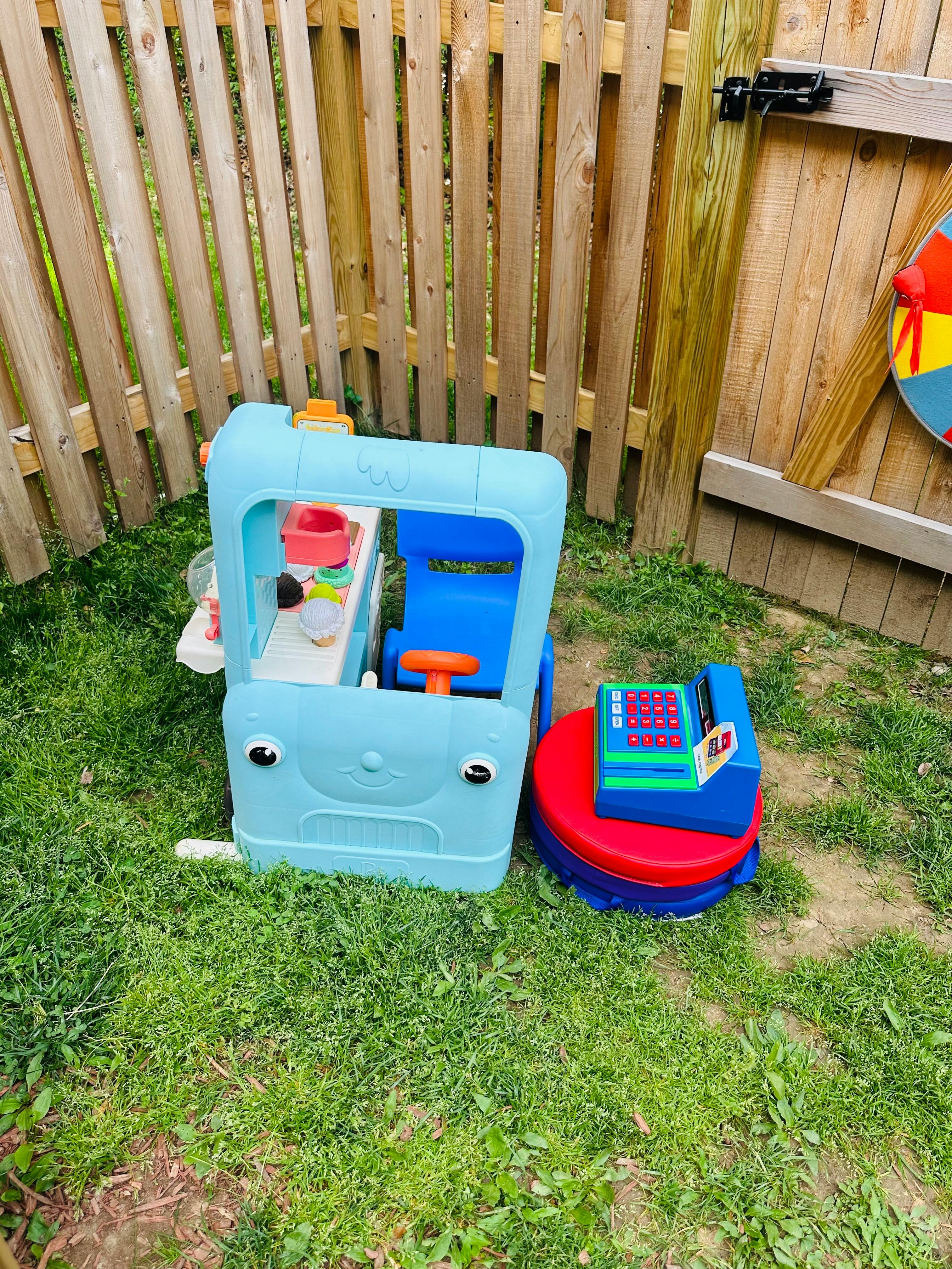 Play food truck and toy cash register on grass next to a wooden fence