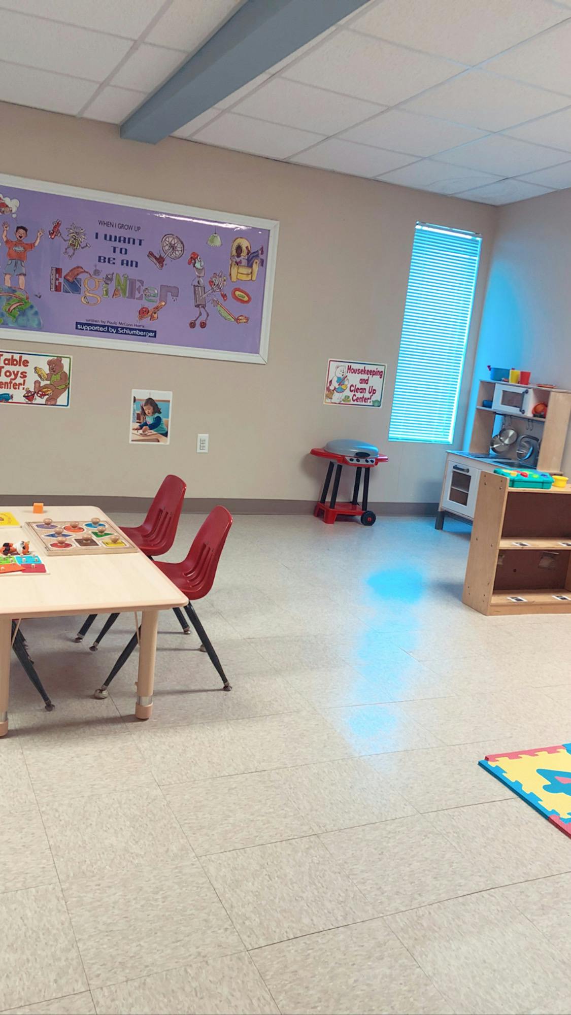 Classroom with small tables and chairs, play kitchen, and wall decorations