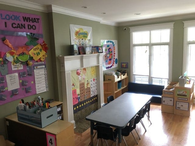 Classroom with a long table and chairs, windows, and children's artwork on walls