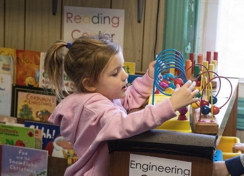 Child playing with a bead maze toy in a classroom