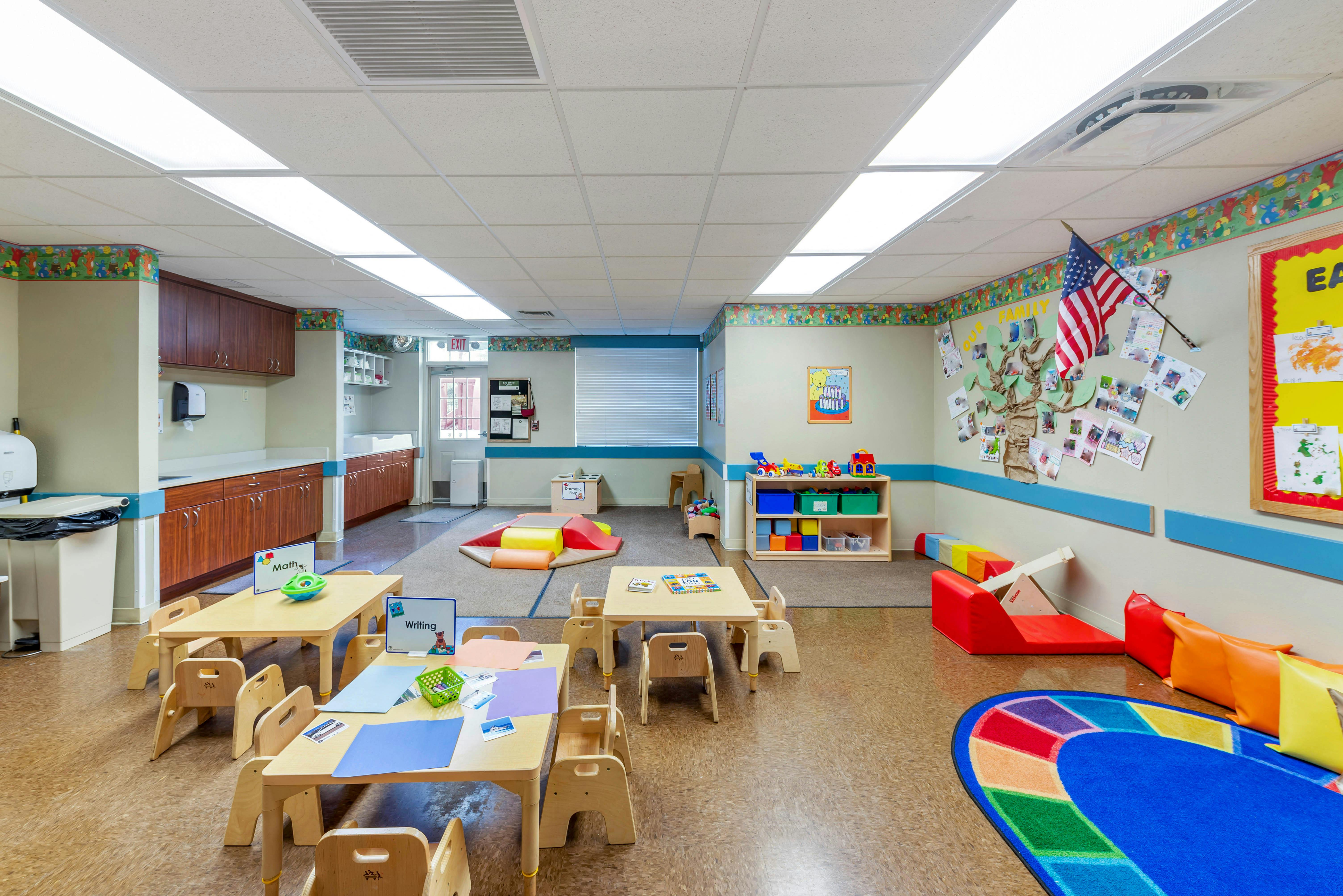 Classroom with small tables and chairs, play mats, and a kitchen area