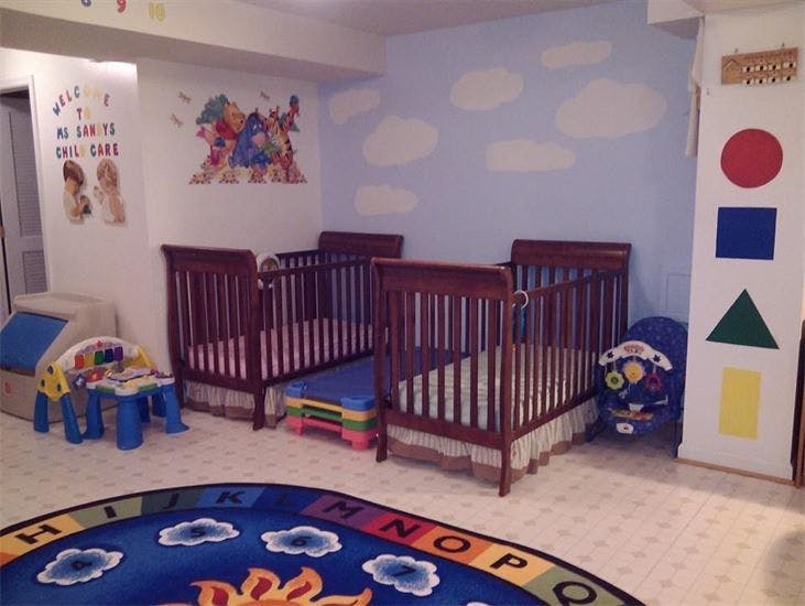 Three cribs in a room with a cloud-painted wall and a colorful rug