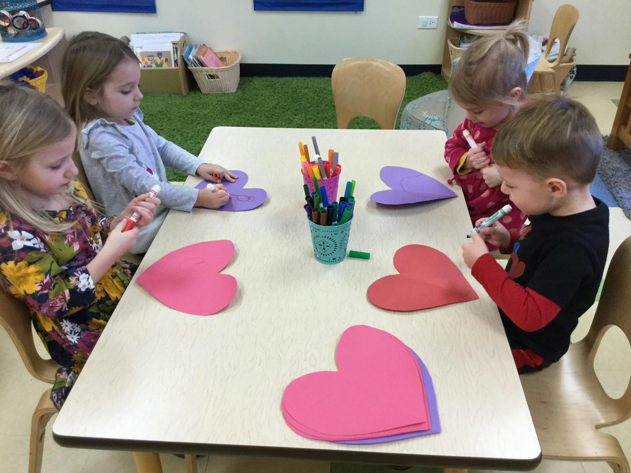Children coloring heart shapes at a table