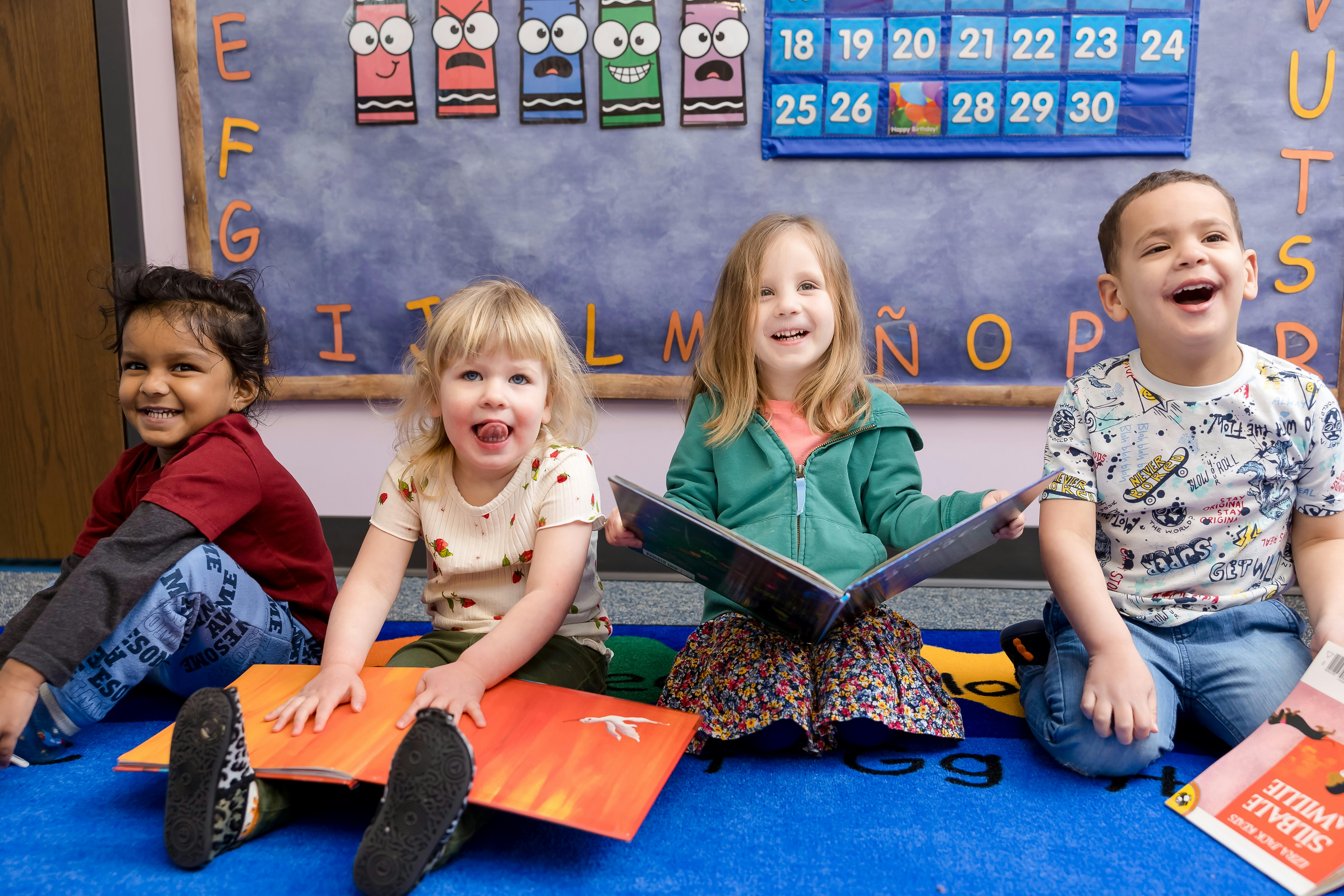 Four children sitting on the floor with books in a classroom