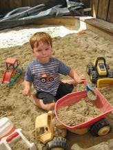 Child playing in sand with toy trucks and shovel