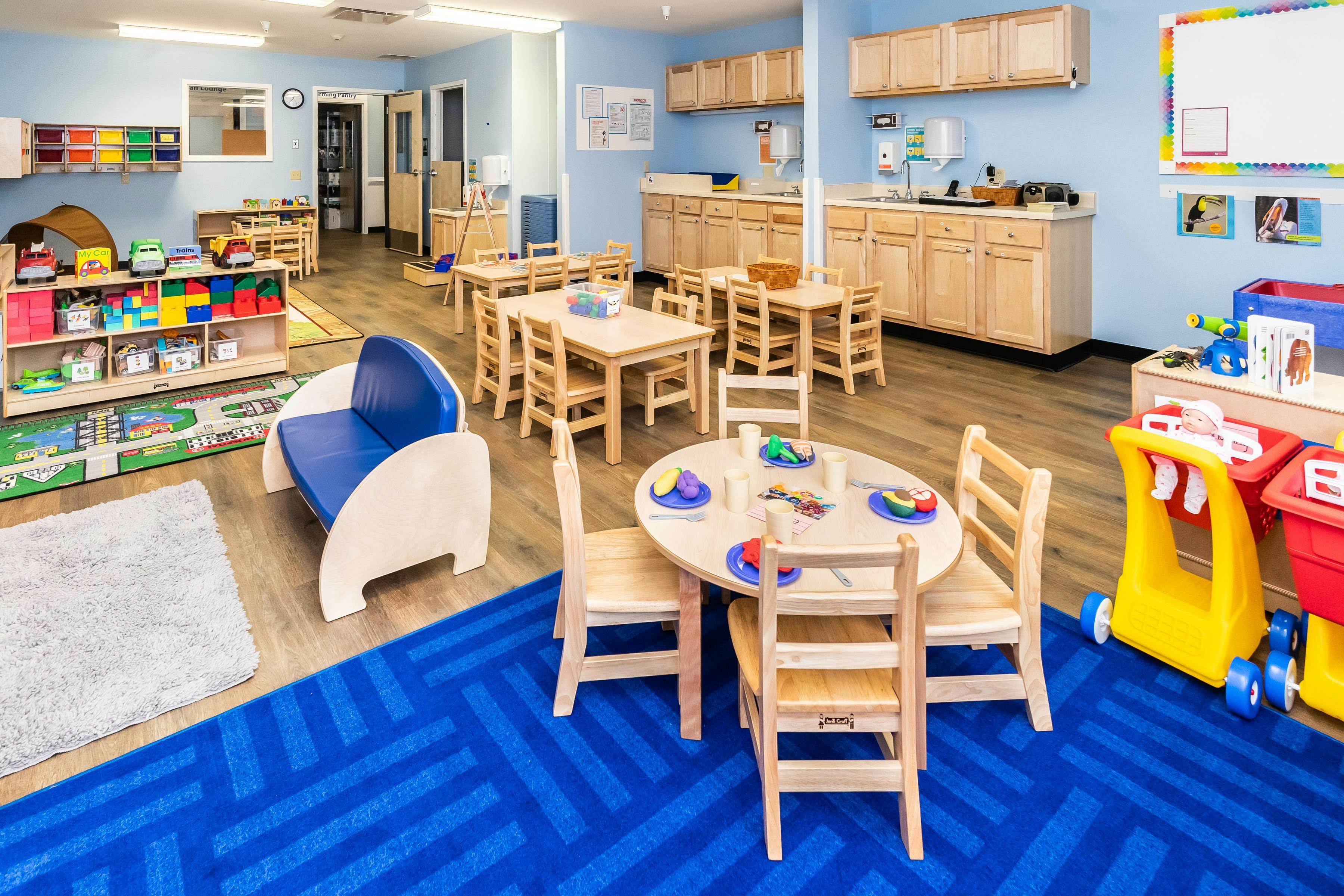 A colorful childcare classroom with various play areas and small tables and chairs