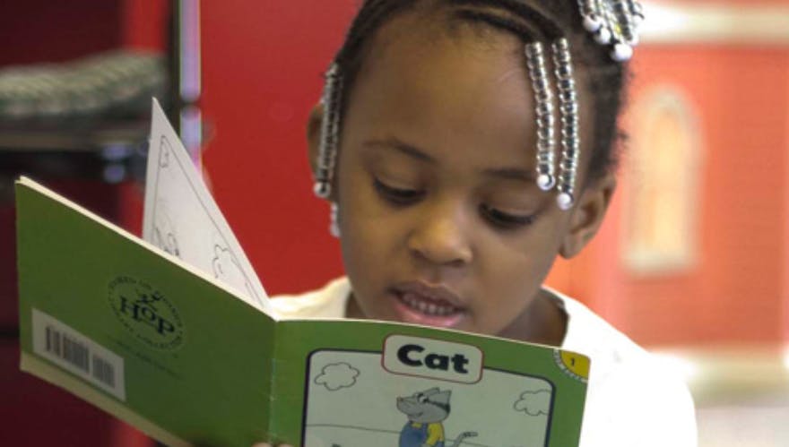 Child reading a book with the word "Cat" on the page