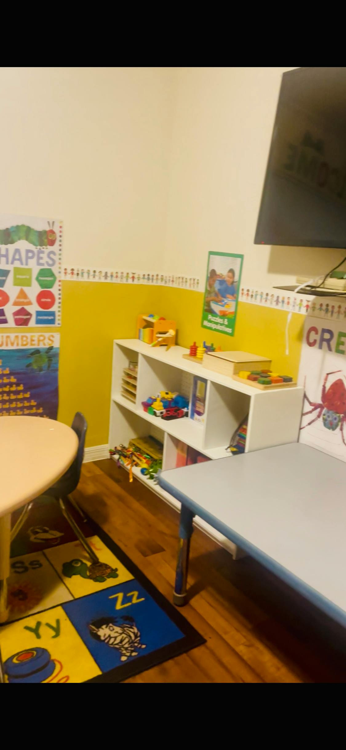 Classroom with tables, shelves of toys, and educational posters