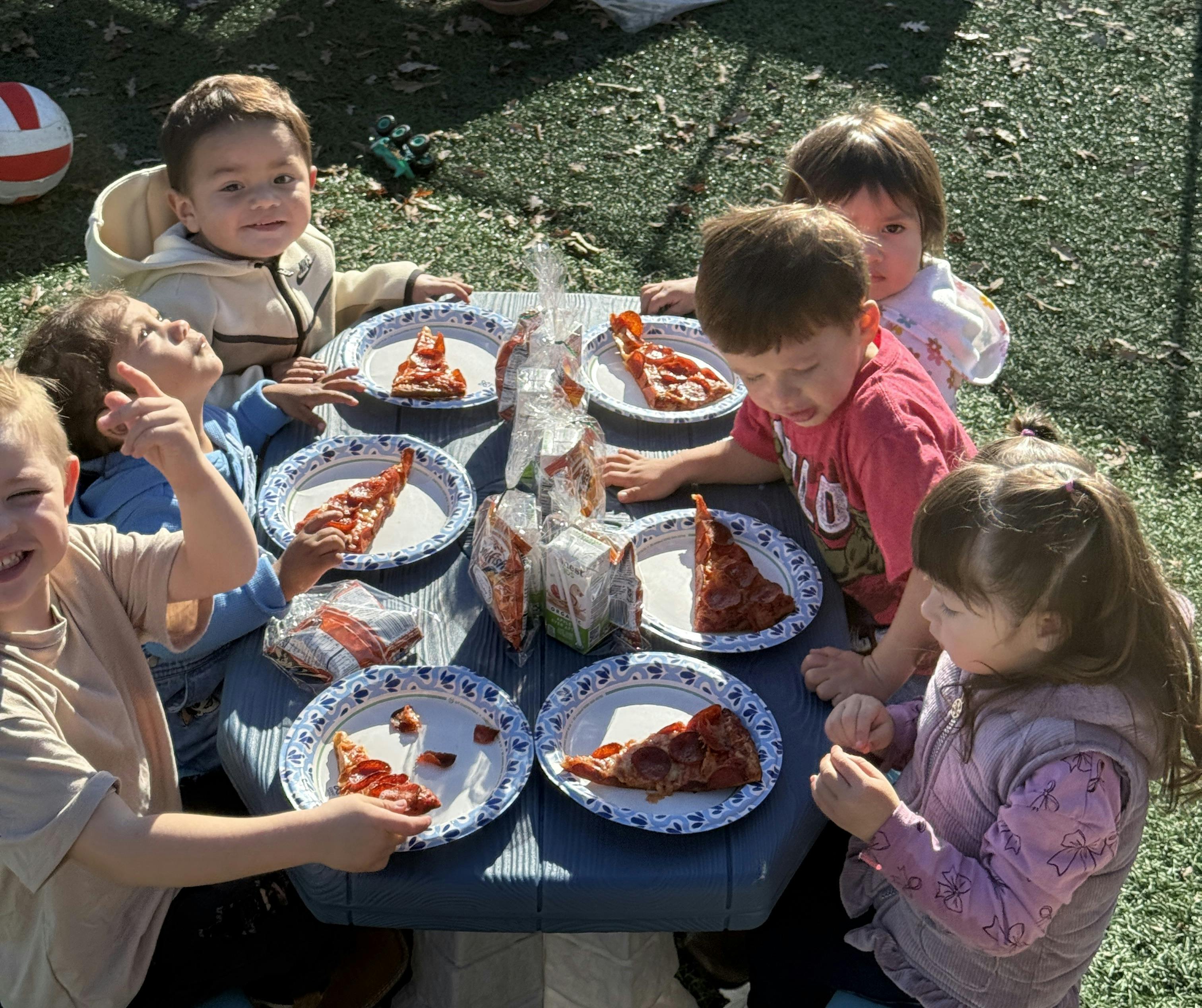 Children eating pizza at a blue picnic table