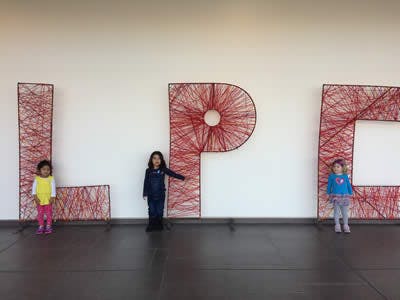 Three children standing in front of large letters made of red string