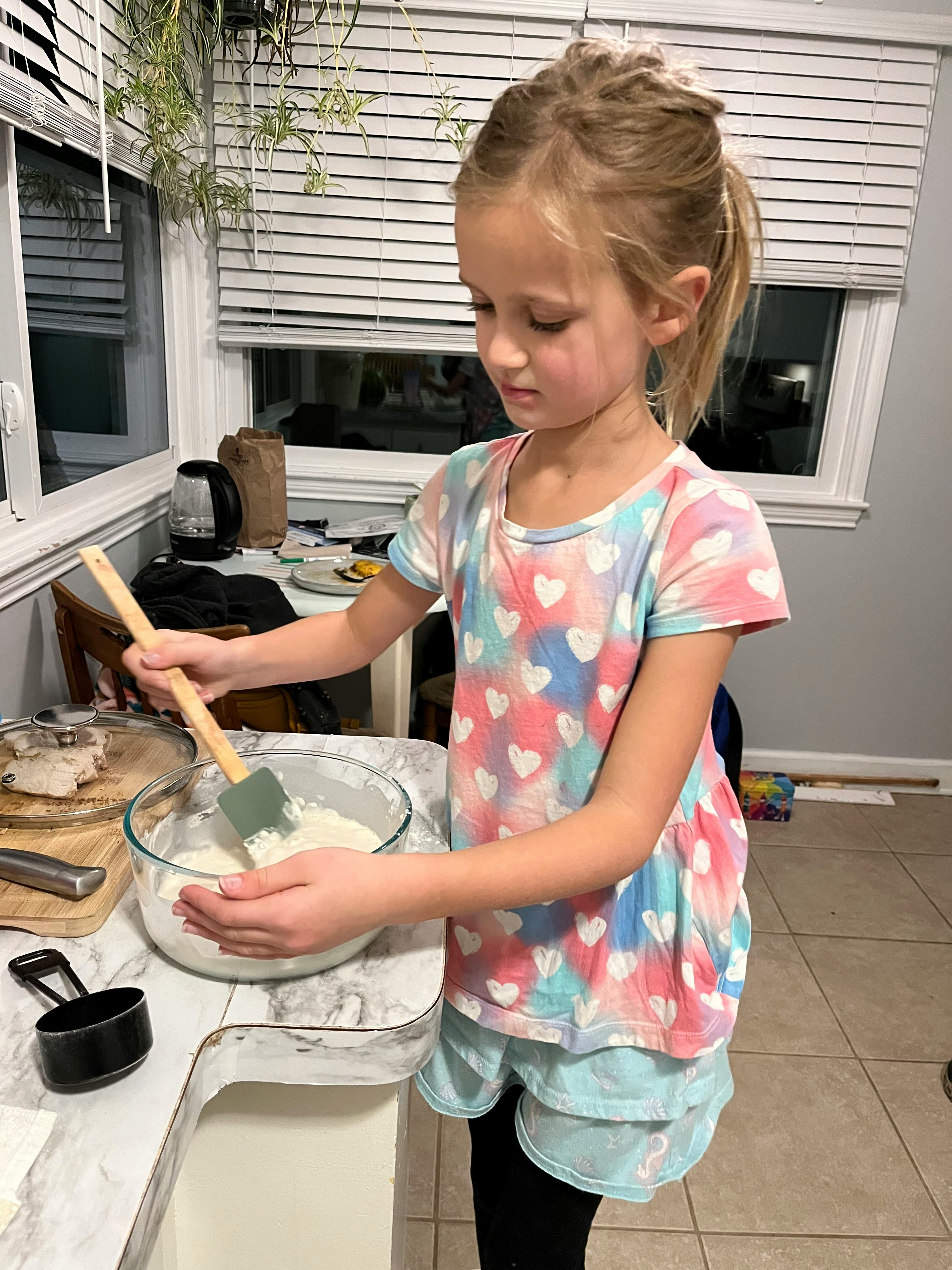 Child stirring a bowl of batter in a kitchen