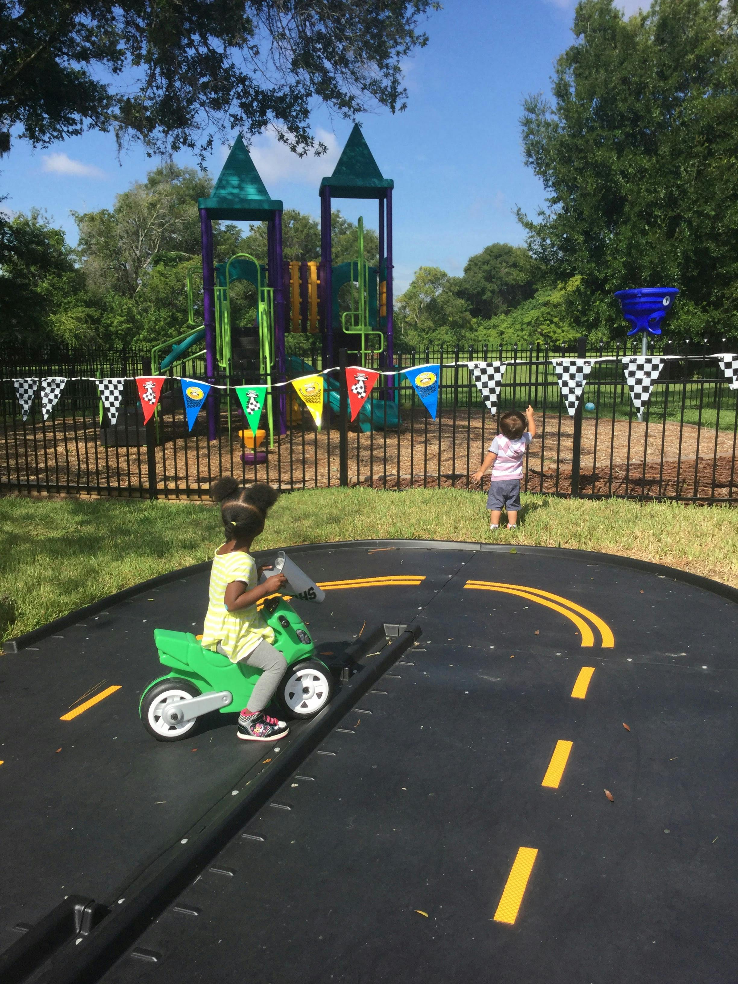 Child on a toy motorcycle on a painted road, another child in background