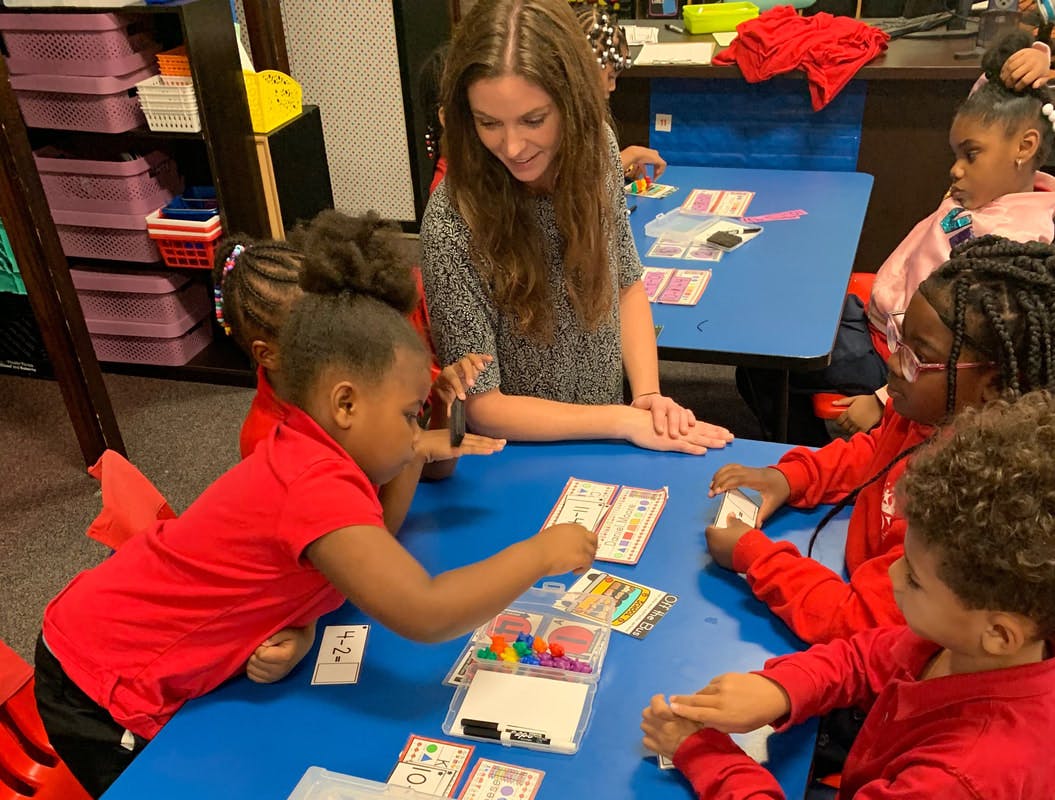 Person and children playing a card game at a blue table