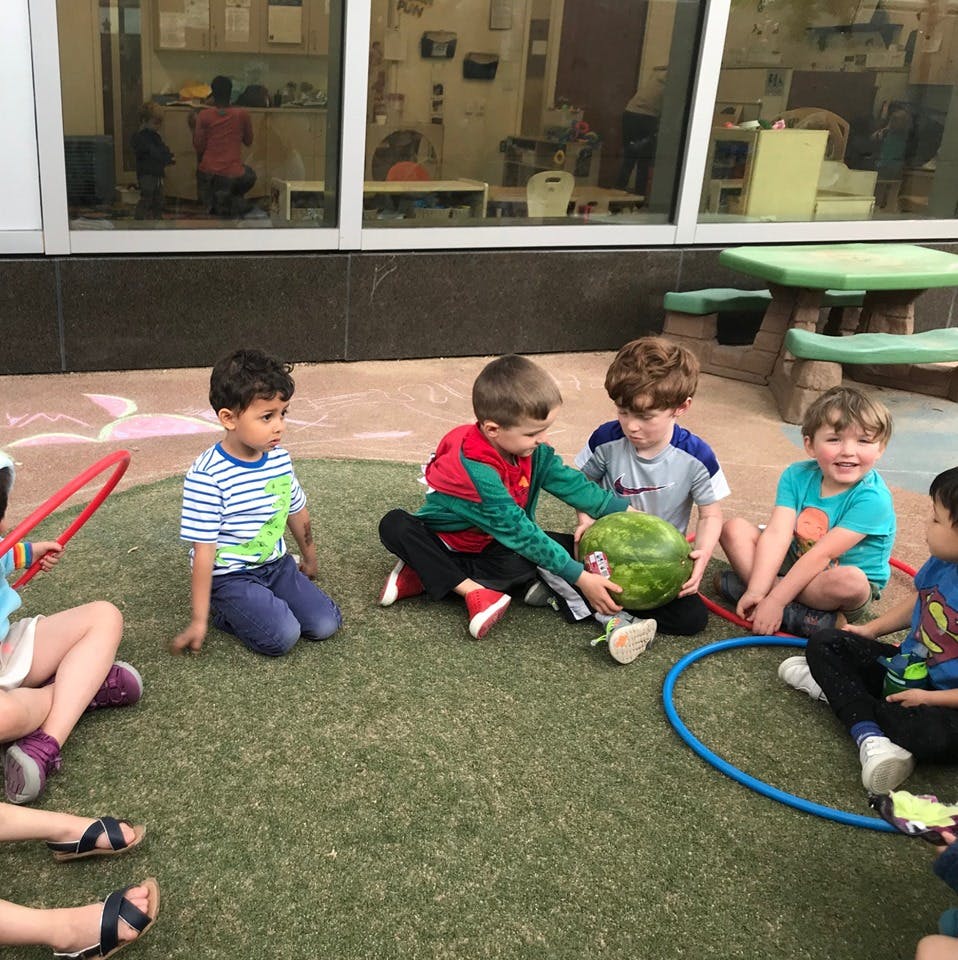 Children sitting on grass with a watermelon and hula hoops