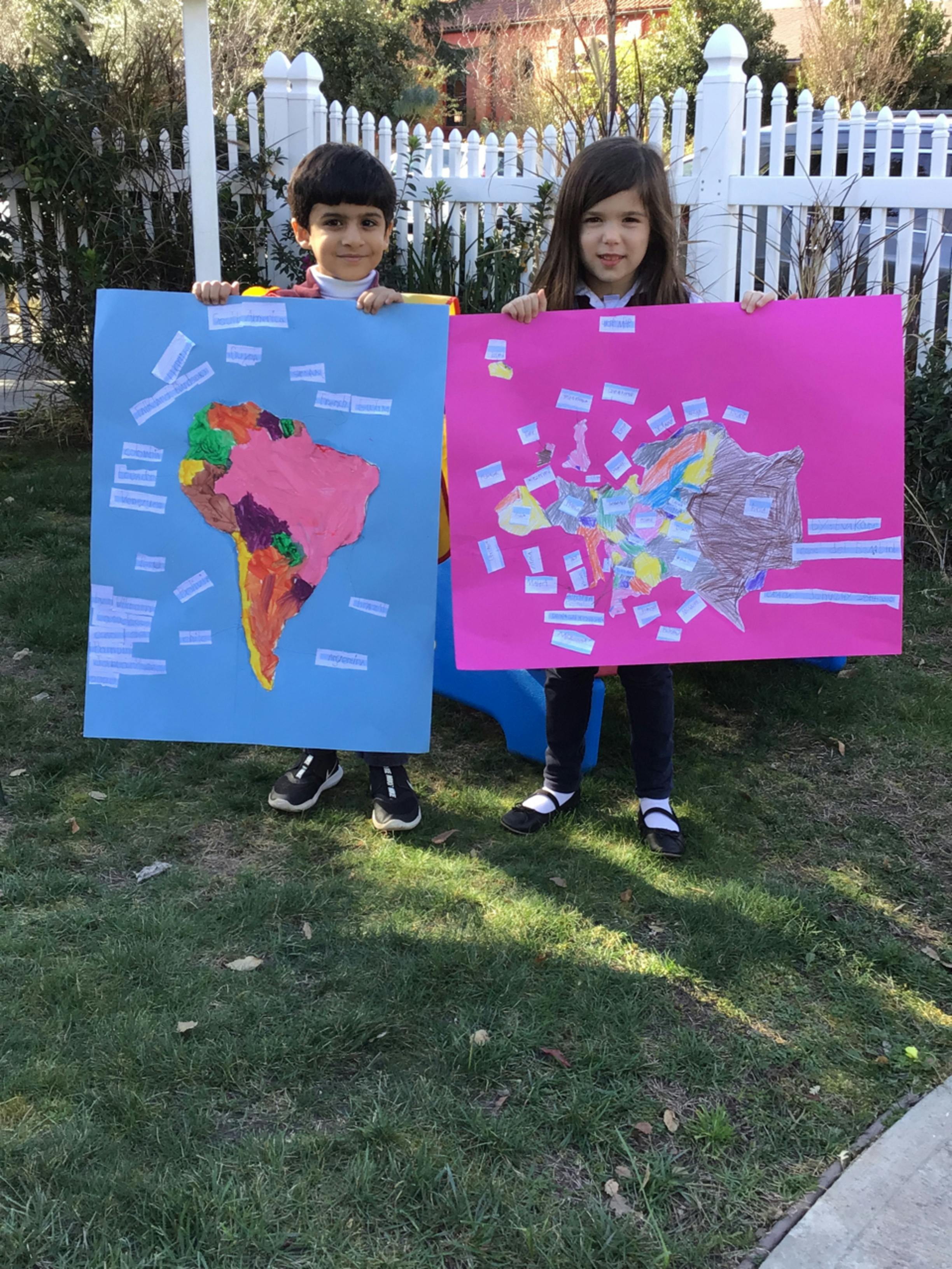 Two children holding up posters with maps drawn on them