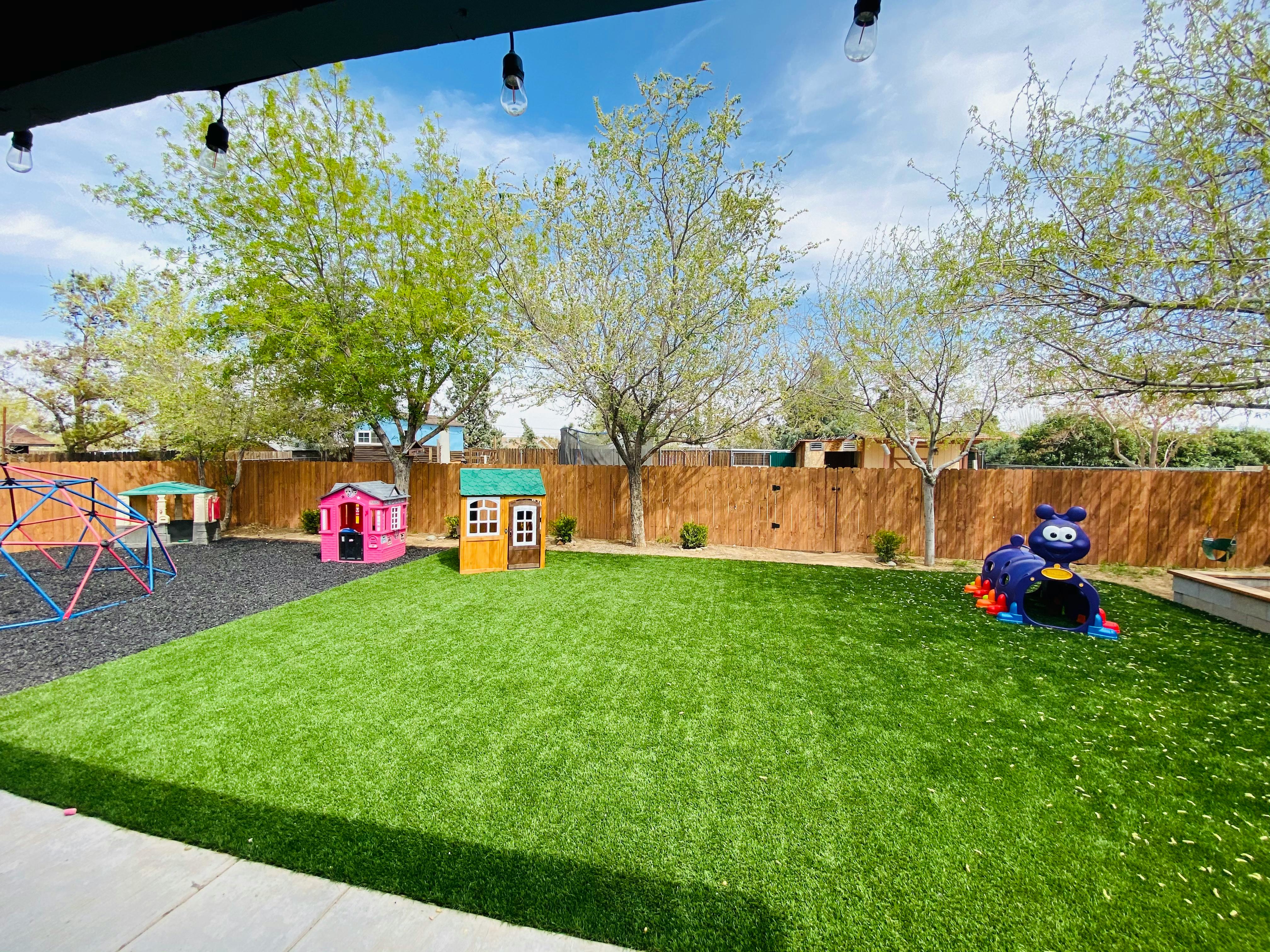 Outdoor play area with artificial turf, playhouses, and climbing structure