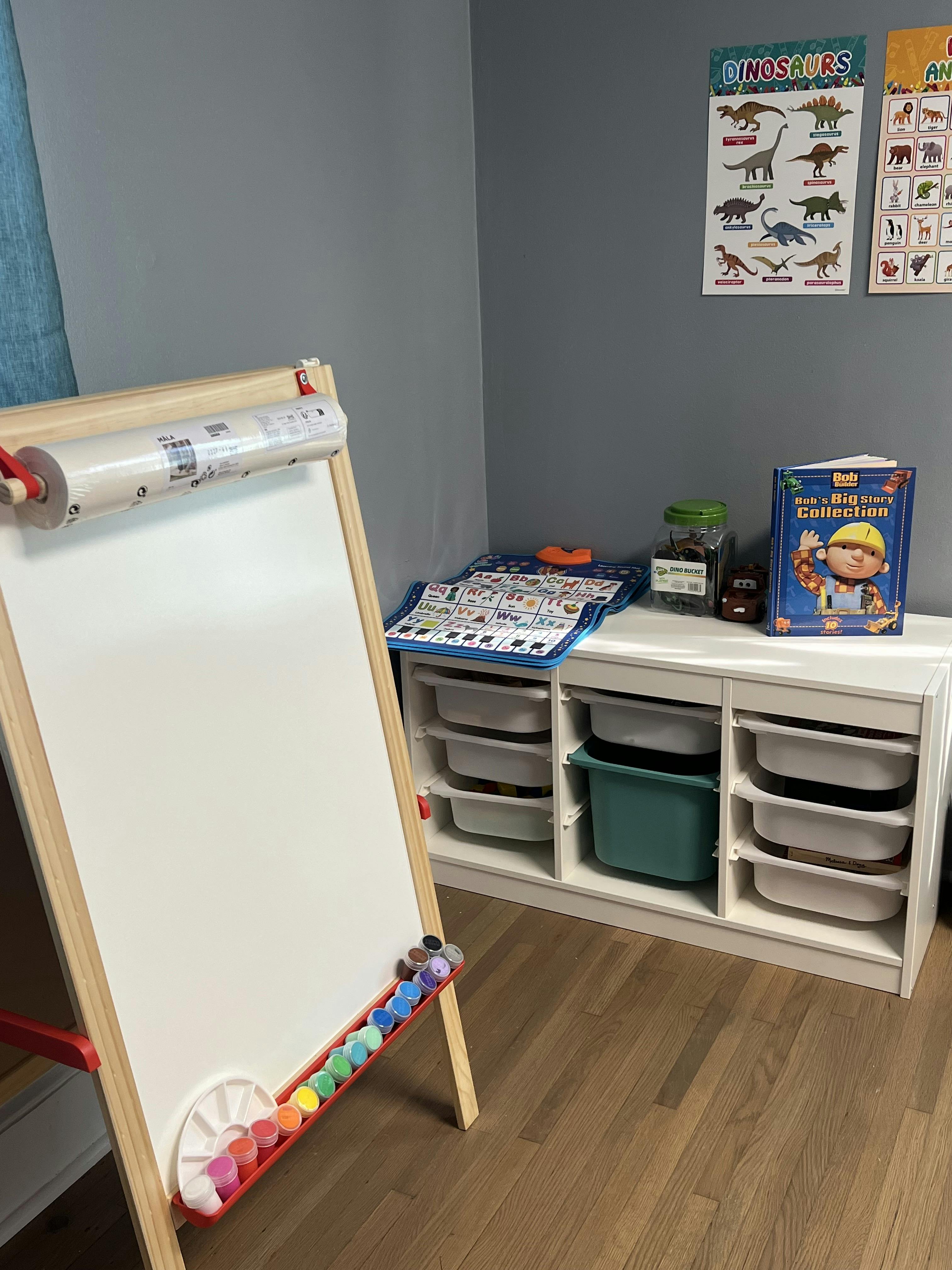 Easel with paper roll and paints next to a storage unit with bins