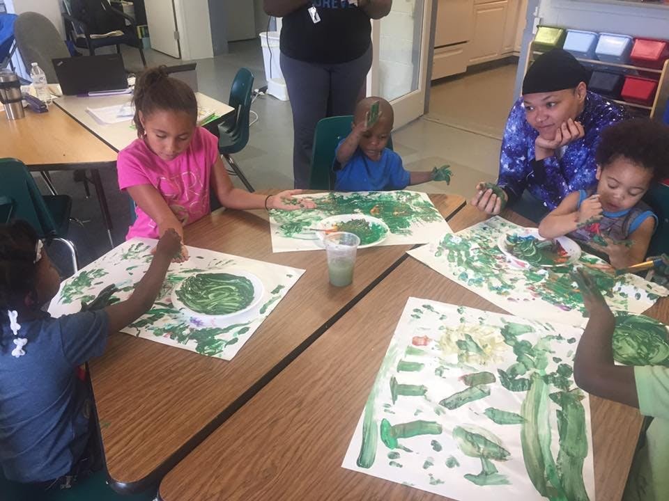Adult and children painting with green paint at a table