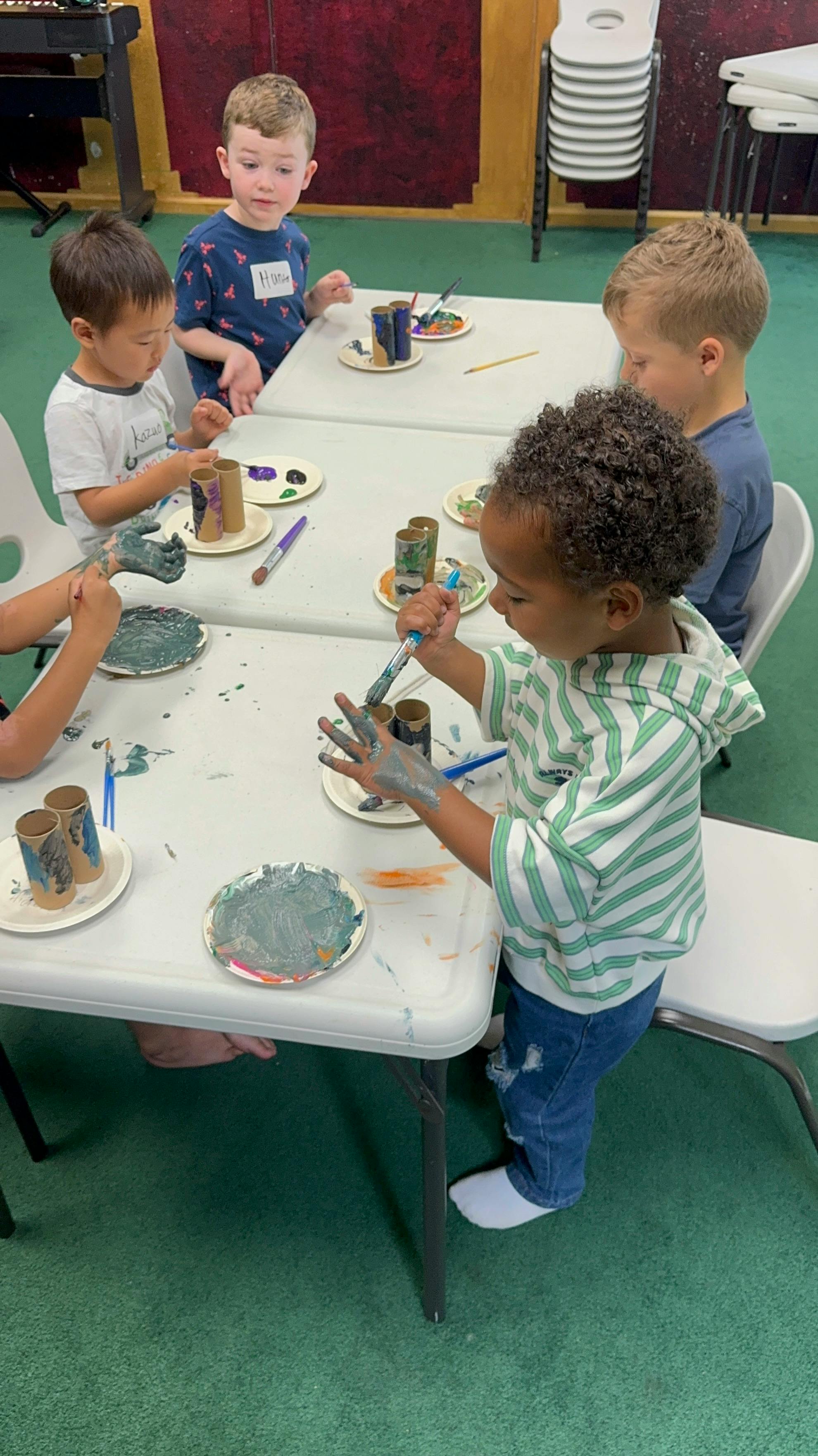 Children painting cardboard tubes with brushes at tables