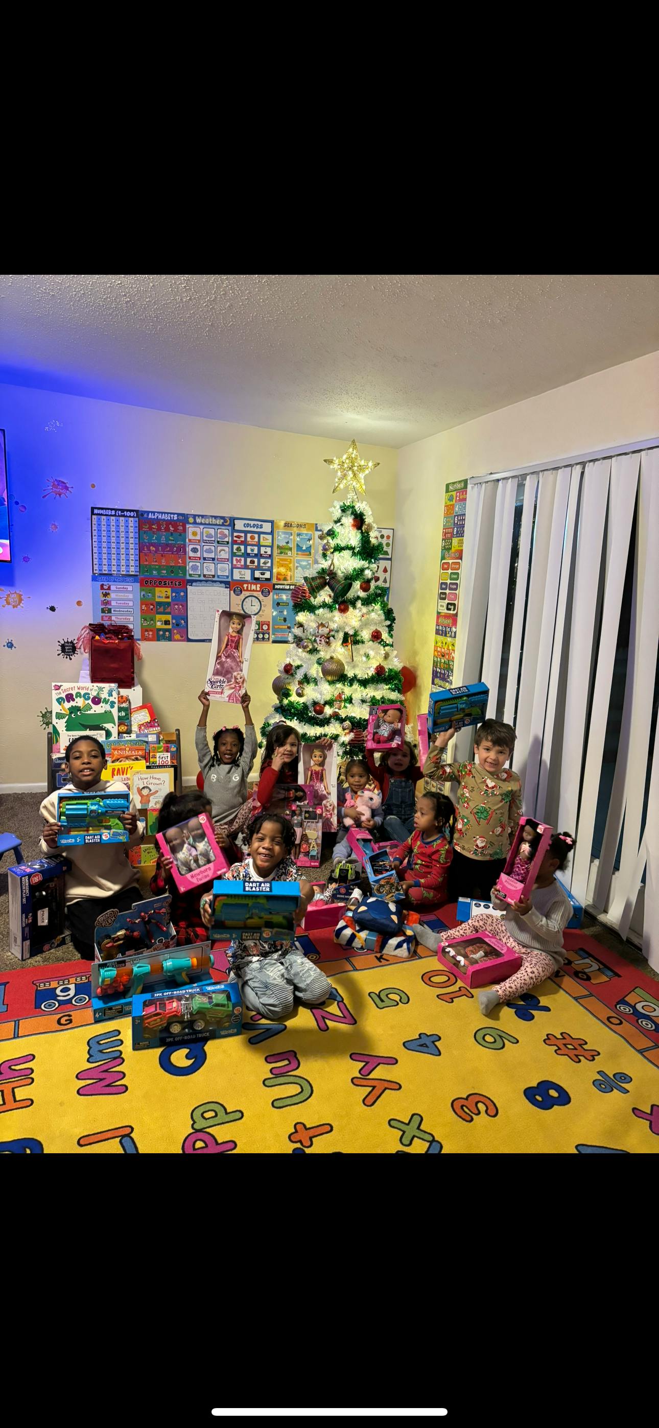 Group of children sitting on a rug with gifts in front of a Christmas tree