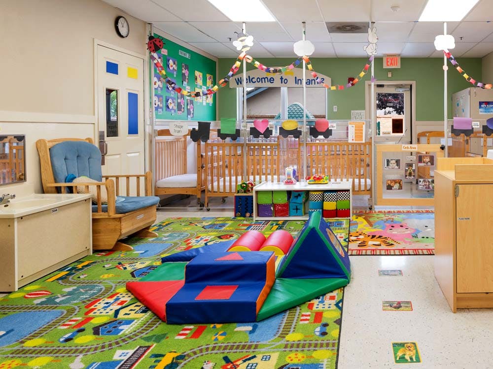 A colorful infant and toddler classroom with play mats, cribs, and soft play equipment