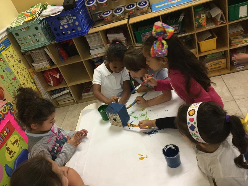 Children painting a birdhouse at a table in a classroom