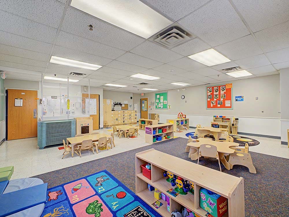 Empty classroom with small tables and chairs, shelves with toys