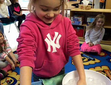 Child in pink hoodie with hands in a bowl